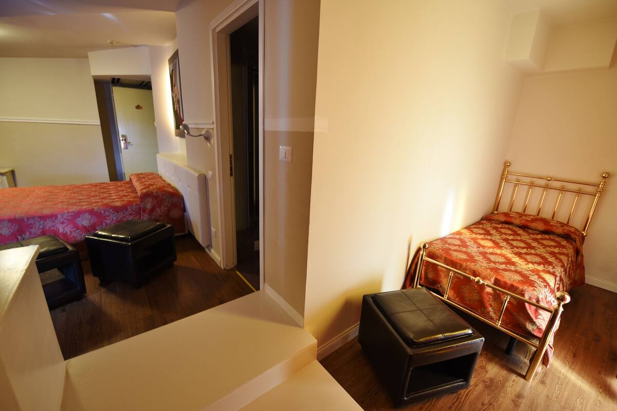 Une chambre avec deux lits, un plancher en bois et une porte donnant sur une autre pièce.