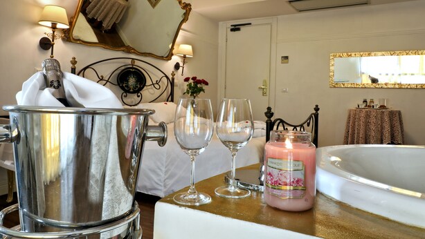 A hotel room with a bed, a large mirror, a bathtub, and a table with a candle and glasses. - Albergo Al Castello (Pomezia)