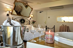 Une chambre d’hôtel avec un lit, un grand miroir, une baignoire et une table sur laquelle se trouvent une bougie et des verres.