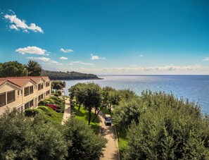 Un hôtel situé sur la côte, offrant une vue sur la mer, doté d’un chemin pavé et entouré d’une végétation luxuriante.