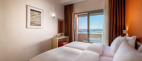 Ett hotellrum med en stor säng, ett litet skrivbord, ett fönster med utsikt över stranden och en inramad tavla på väggen.