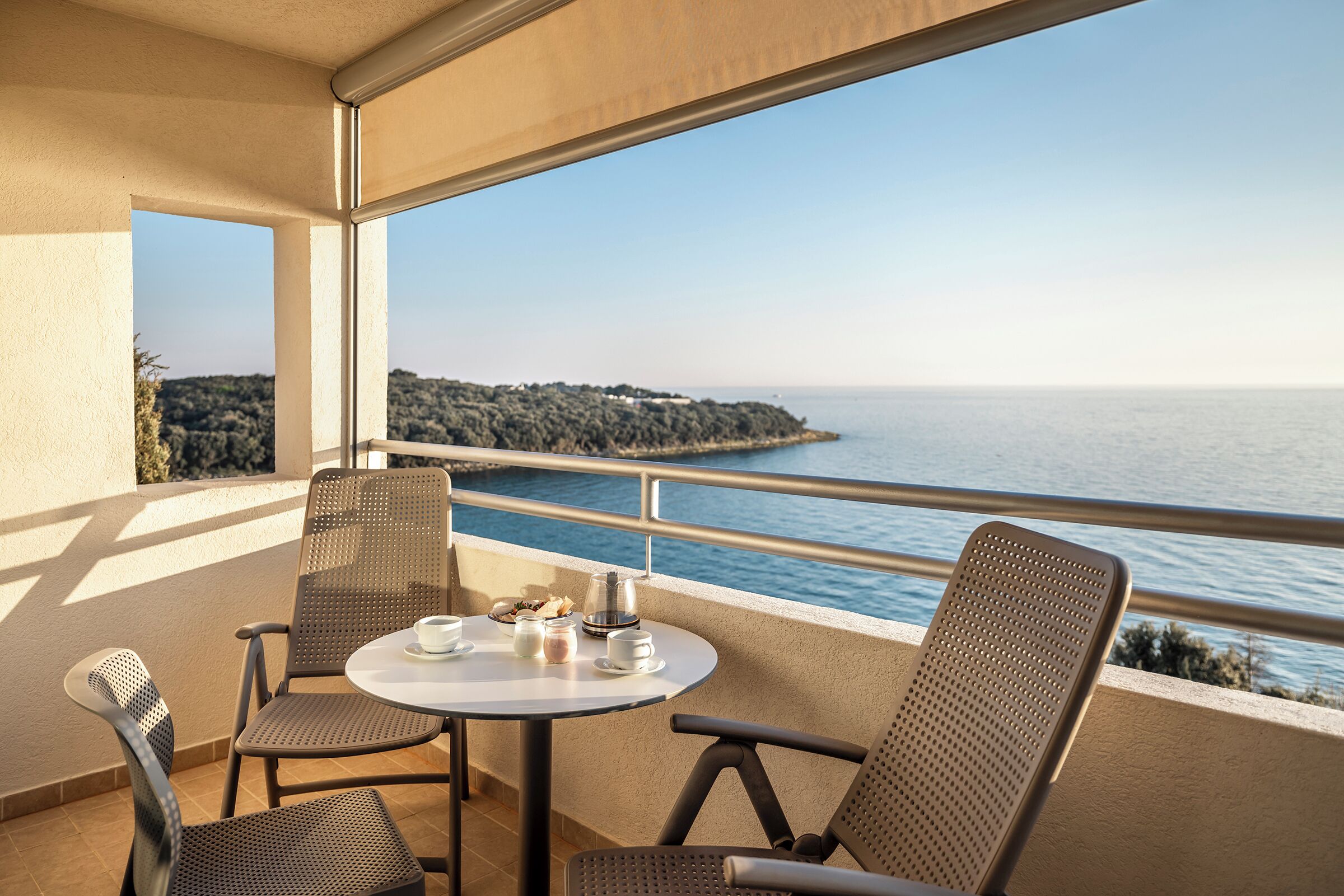A balcony with a table and chairs, overlooking a body of water and a distant shoreline.