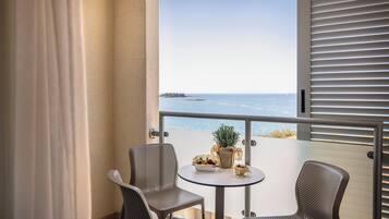 A balcony with two chairs, a small table, and a potted plant. The balcony overlooks a body of water and a distant landmass.