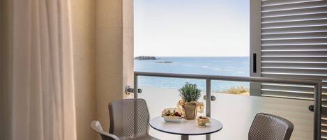 A balcony with two chairs, a small table, and a potted plant. The balcony overlooks a body of water and a distant landmass.