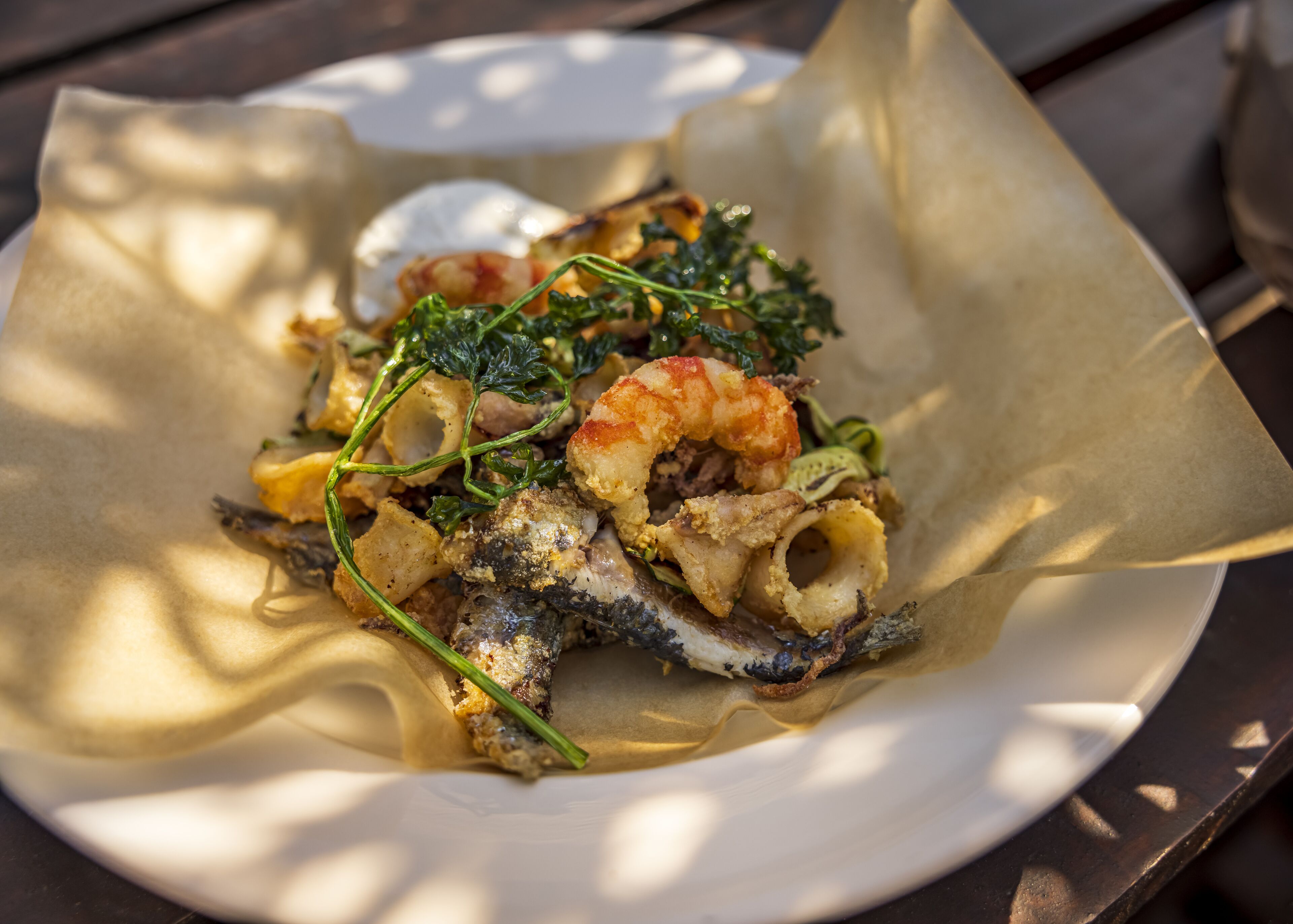 A plate of food with seafood, including shrimp and squid, served on a white plate with a paper liner.