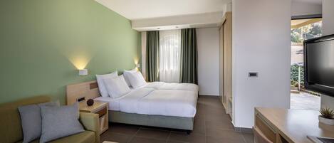 Une chambre d’hôtel moderne équipée d’un lit, d’un canapé, d’une télévision et d’une petite table sur laquelle se trouve un panier de fruits.