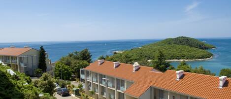 Ein Küstenhotel mit mehreren Balkonen, Blick auf das Meer und einer kleinen Insel in der Ferne.