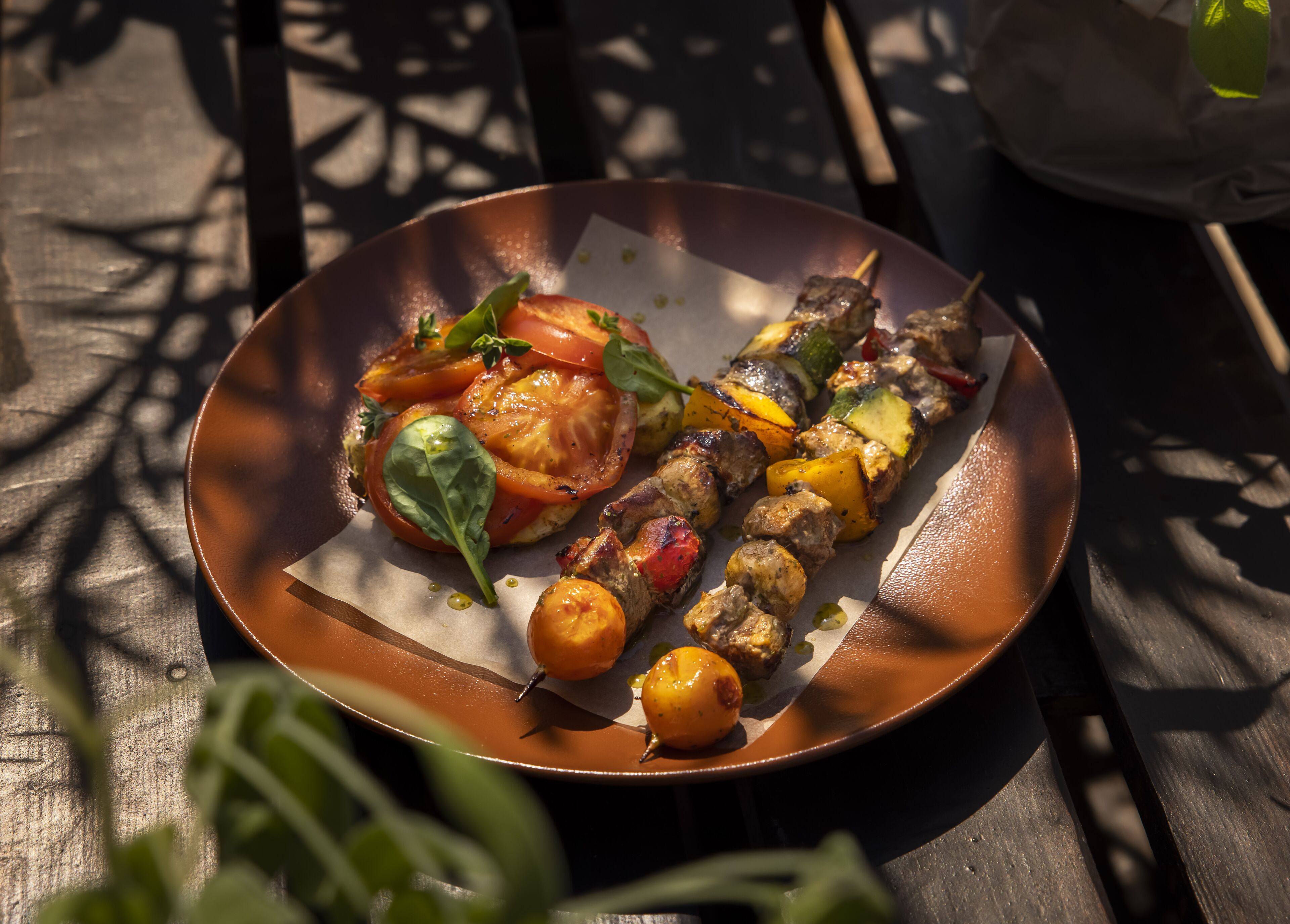 Um prato com legumes grelhados e espetinhos de carne sobre uma mesa de madeira.