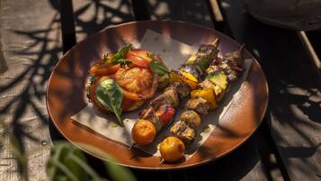 Um prato com legumes grelhados e espetinhos de carne sobre uma mesa de madeira.