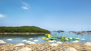 Une plage avec des chaises longues et des parasols, un bateau et, au loin, une île couverte de forêt.