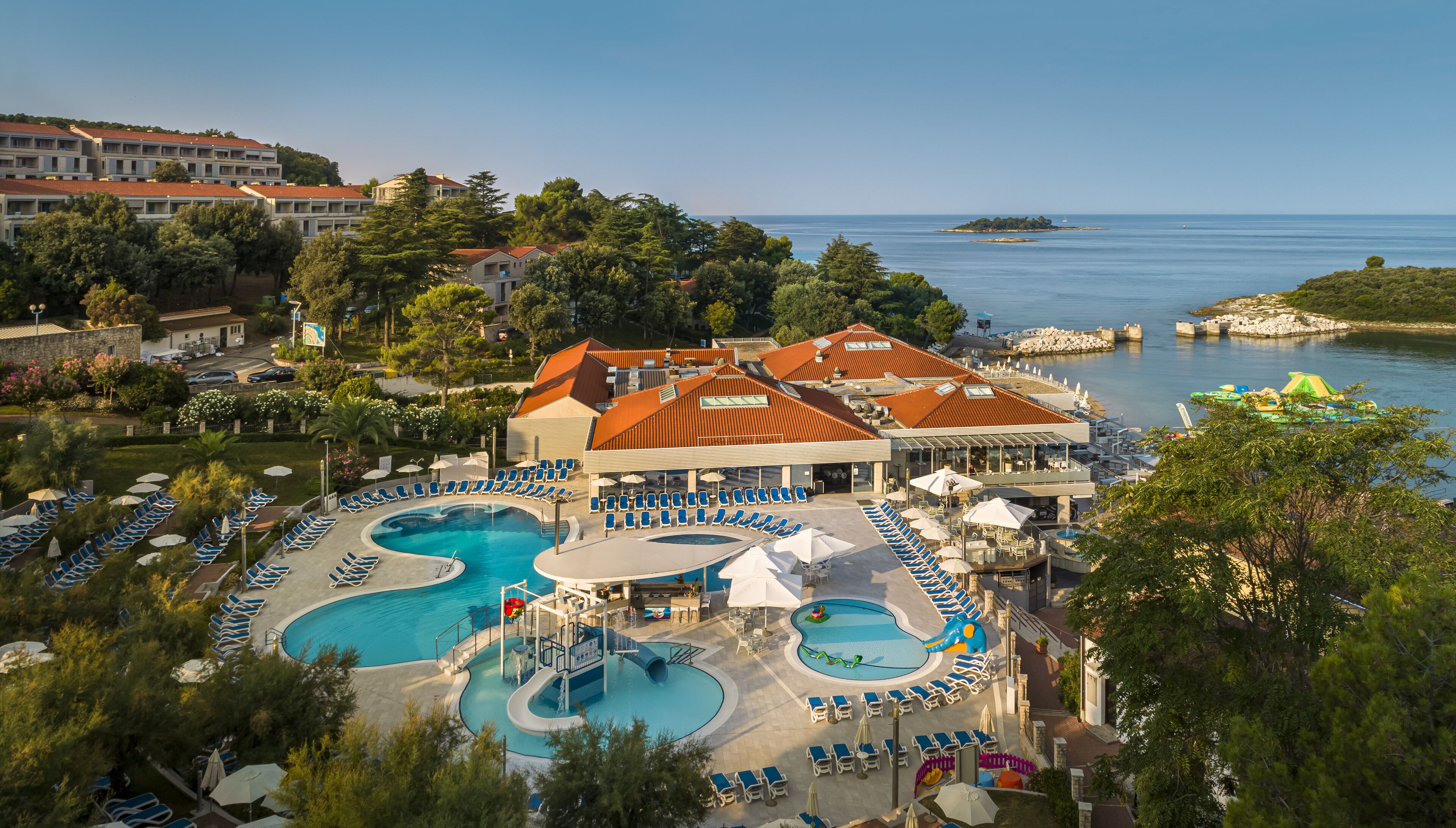 Un resort con varias piscinas, un edificio grande de techo rojo y vistas al mar.