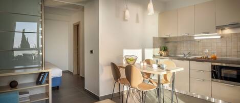 A modern kitchen with a dining area, featuring a breakfast bar, a coffee machine, and a view of the city through a large window.