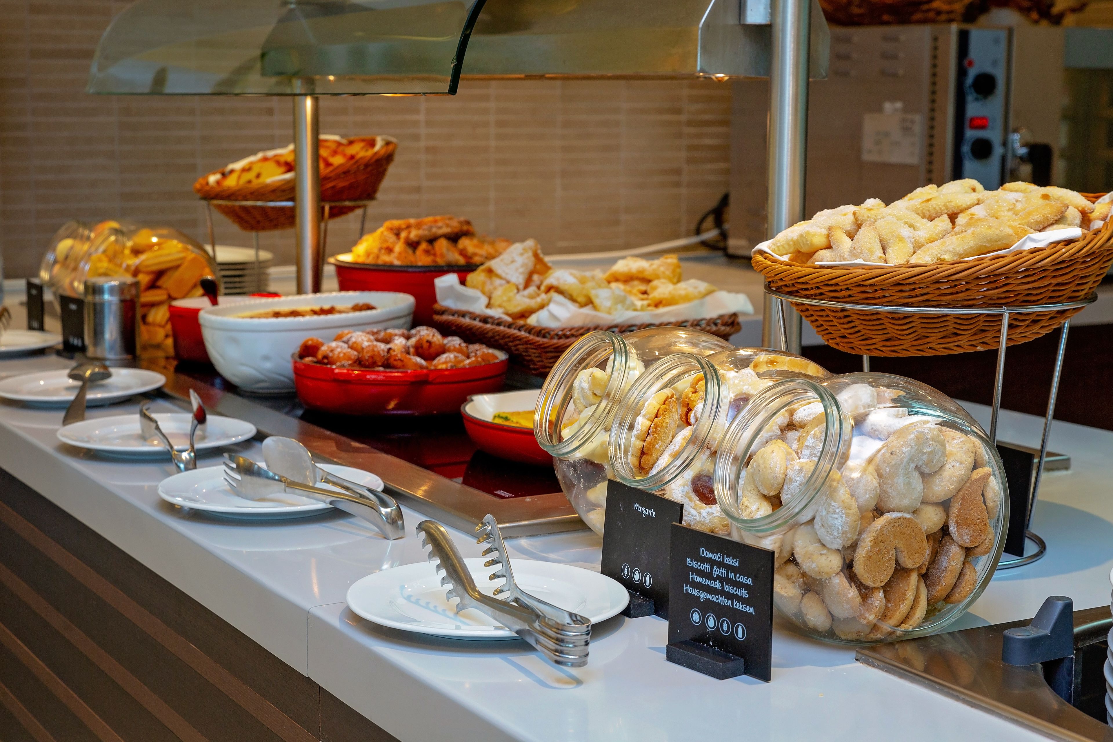 A buffet with various food items, including pastries and desserts, arranged on a counter with serving utensils and plates.