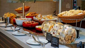 A buffet with various food items, including pastries and desserts, arranged on a counter with serving utensils and plates.