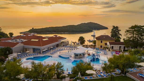 Un complexe hôtelier doté de plusieurs piscines, de chaises longues et offrant une vue sur la mer au coucher du soleil.