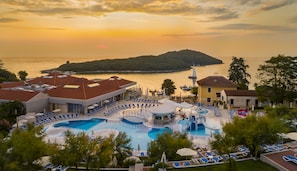 Un resort con varias piscinas, sillones de sol y vista al mar al atardecer.