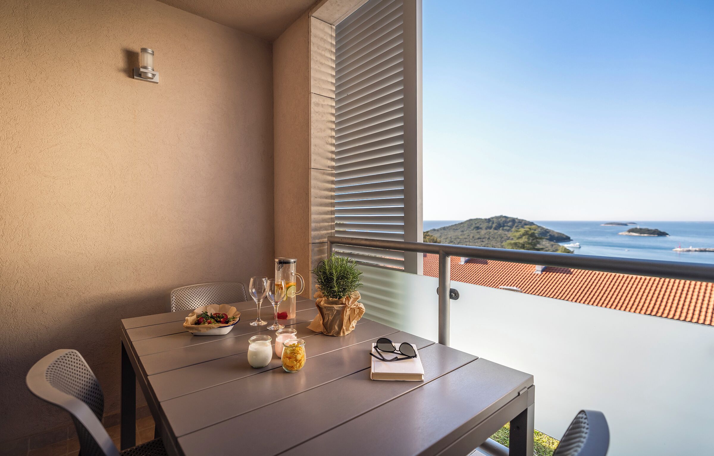A balcony with a table set for dining, a potted plant, and a view of the sea.