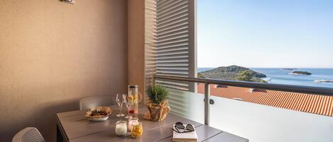 A balcony with a table set for dining, a potted plant, and a view of the sea.