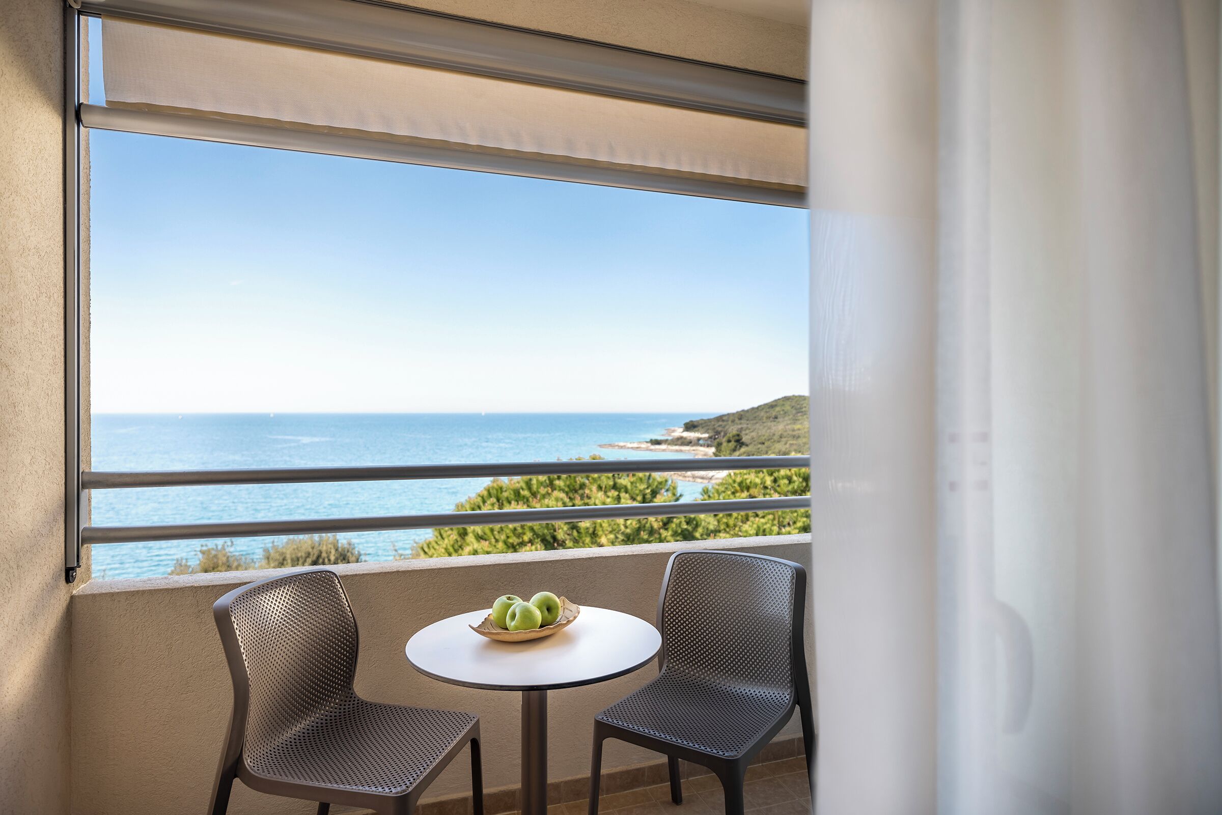 Un balcone con vista sul mare, due sedie e un tavolo con una ciotola di mele.