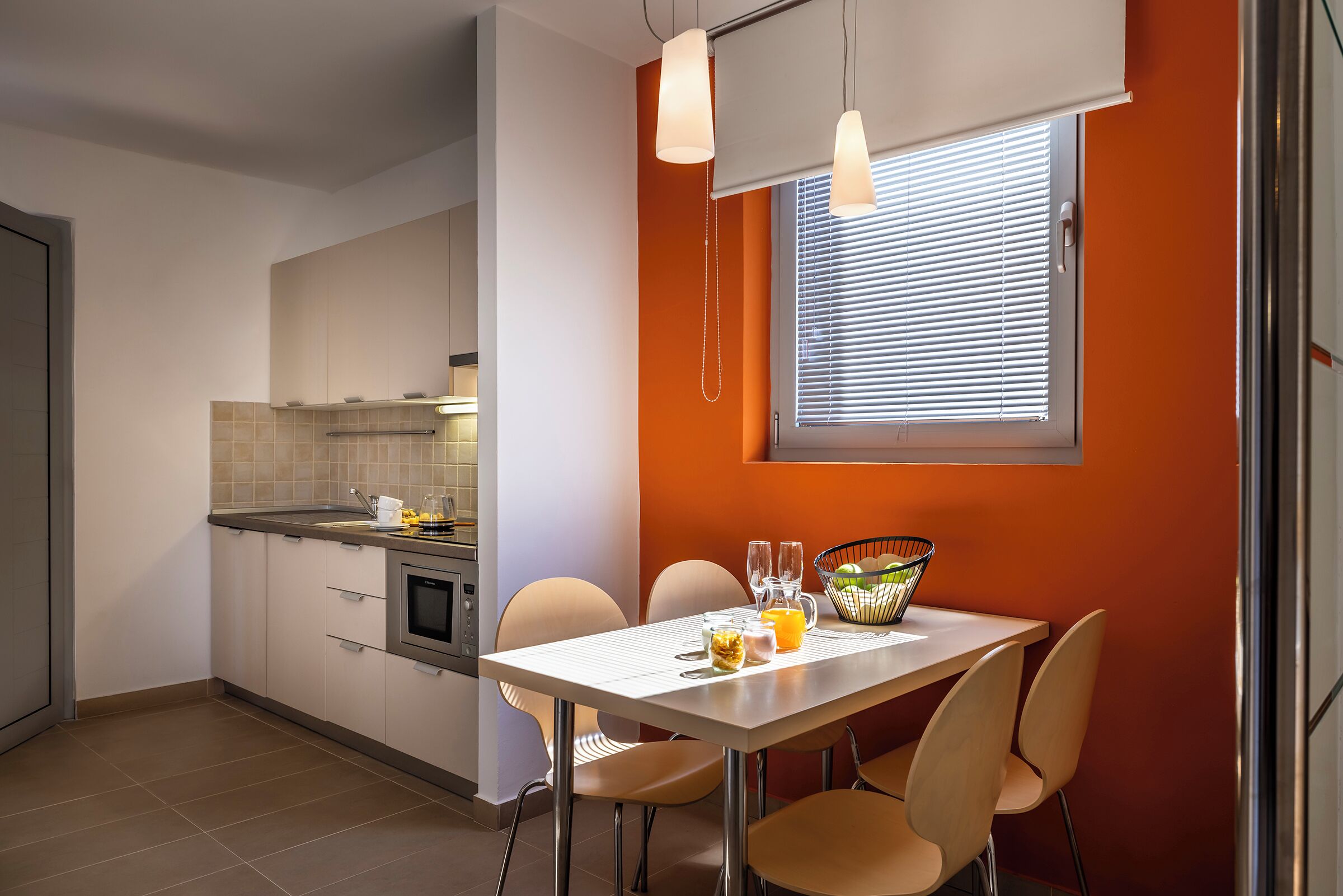 Een moderne keuken met witte kasten, een eettafel met stoelen en een raam met zonwering.