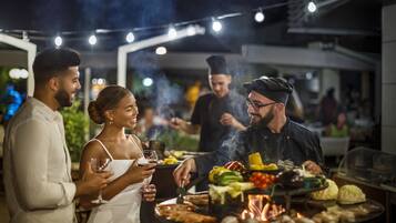 Een groep mensen eet buiten in de avond, met een barbecue en verschillende gerechten.
