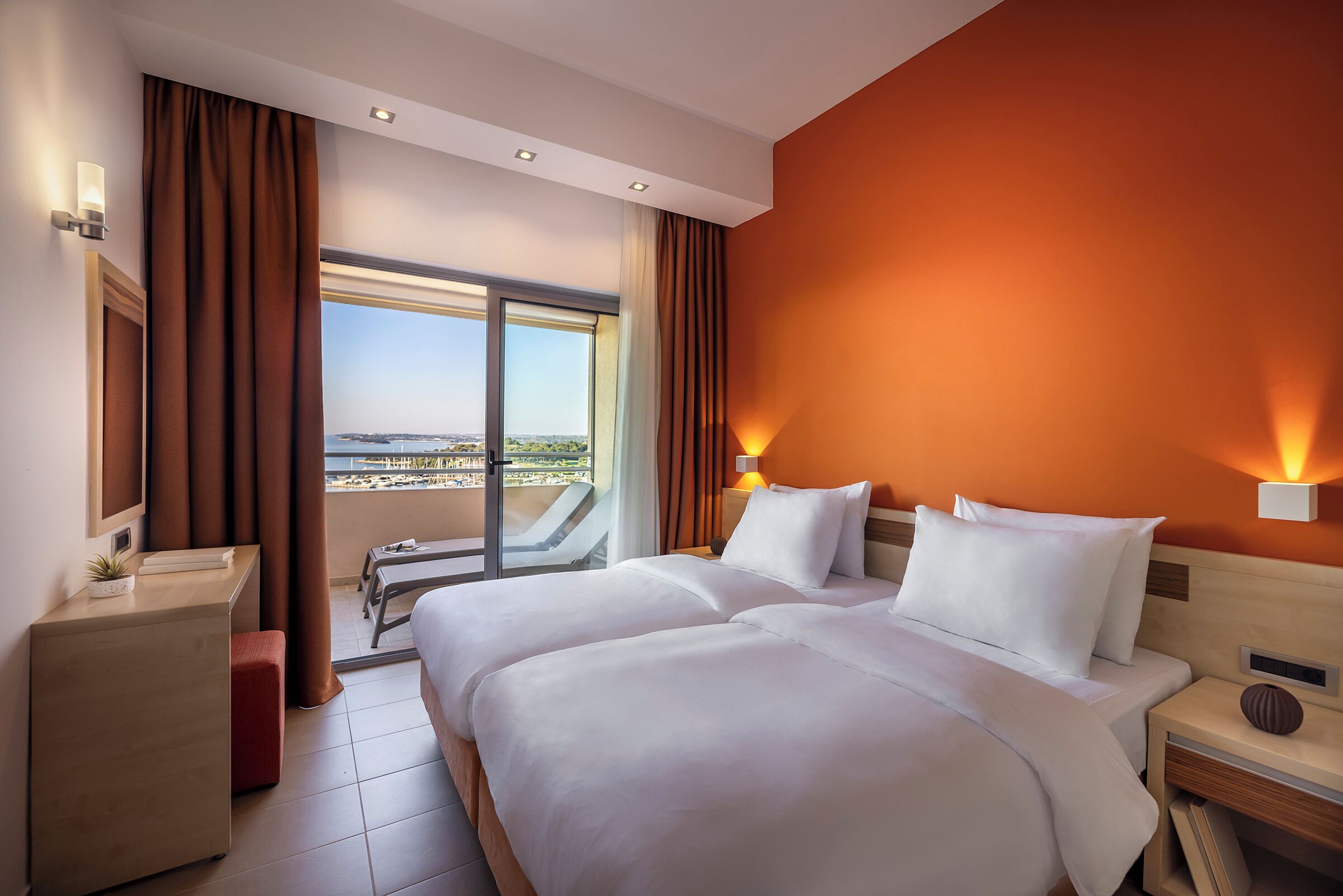Habitació d'hotel amb un llit gran, un escriptori, una cadira i vista a la ciutat a través d'una finestra ampla.