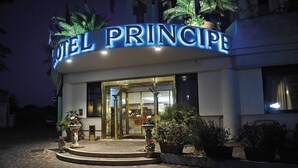 En hotelindgang med et skilt, der viser "HOTEL PRINCIPE", med en buet facade, glasdøre og plantekasser.