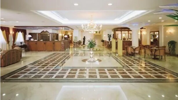 En rummelig hotellobby med en central springvand, en receptionsdisk og et spiseområde med stole og borde.