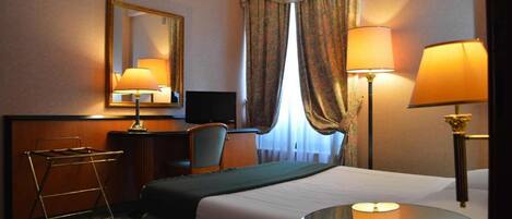 A hotel room with a bed, a desk, a chair, a television, and two lamps.