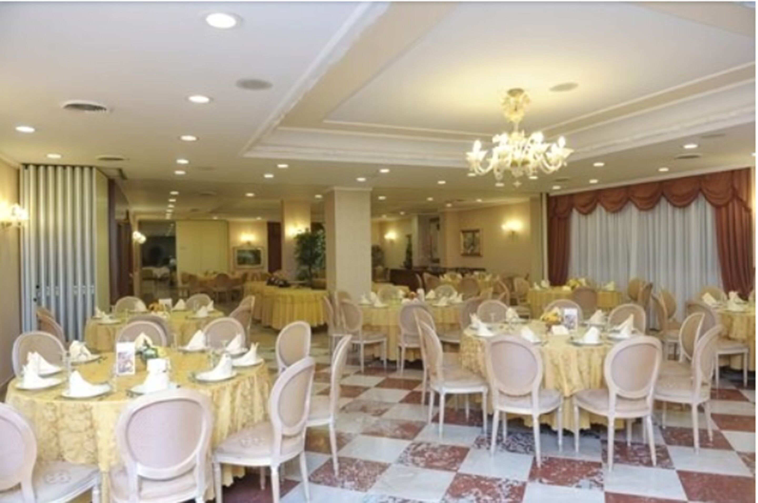 Un salón de banquetes con mesas redondas dispuestas para cenar, sillas blancas y una araña de cristal.