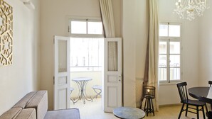 Une pièce comprenant un canapé, une table à manger avec des chaises, un lustre et une vue sur l’extérieur par une porte ouverte.