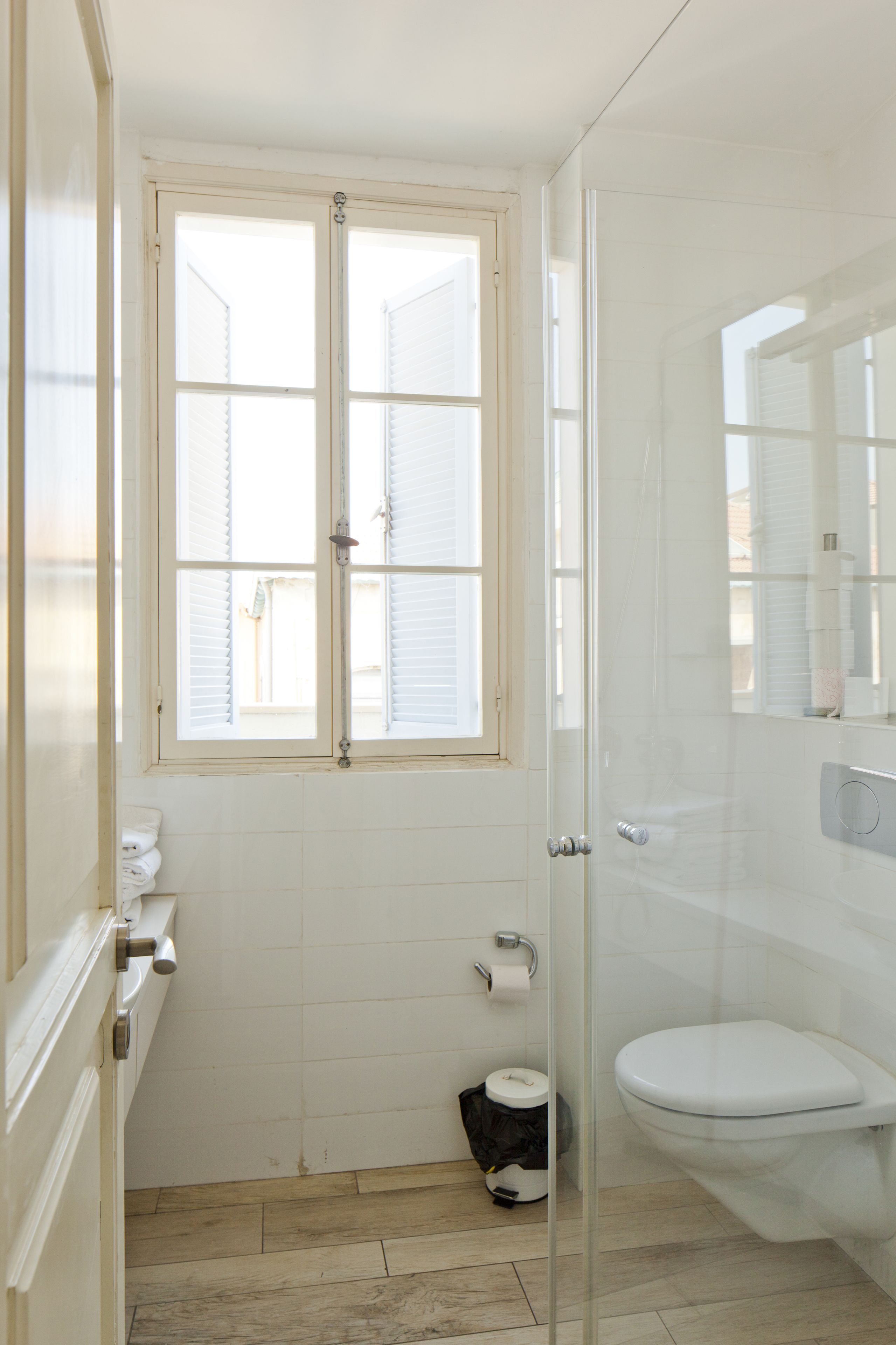 A bathroom with a toilet, a glass shower enclosure, a window with blinds, and a towel rack.