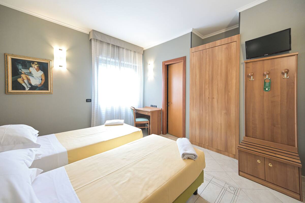 A hotel room with two beds, a desk, a chair, a wardrobe, and a television.