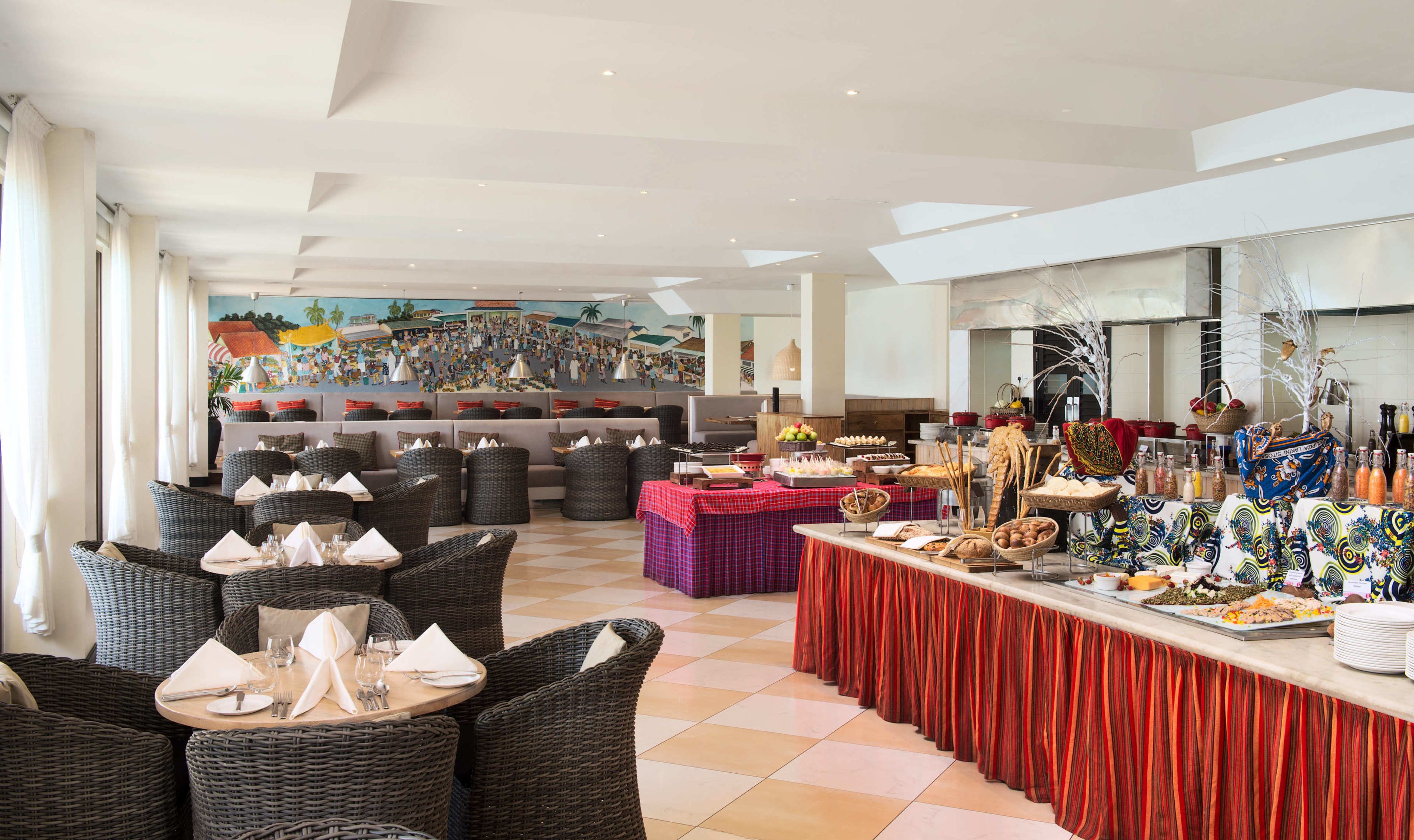 Un espace repas avec des meubles en osier, un buffet proposant divers plats et une fresque murale.