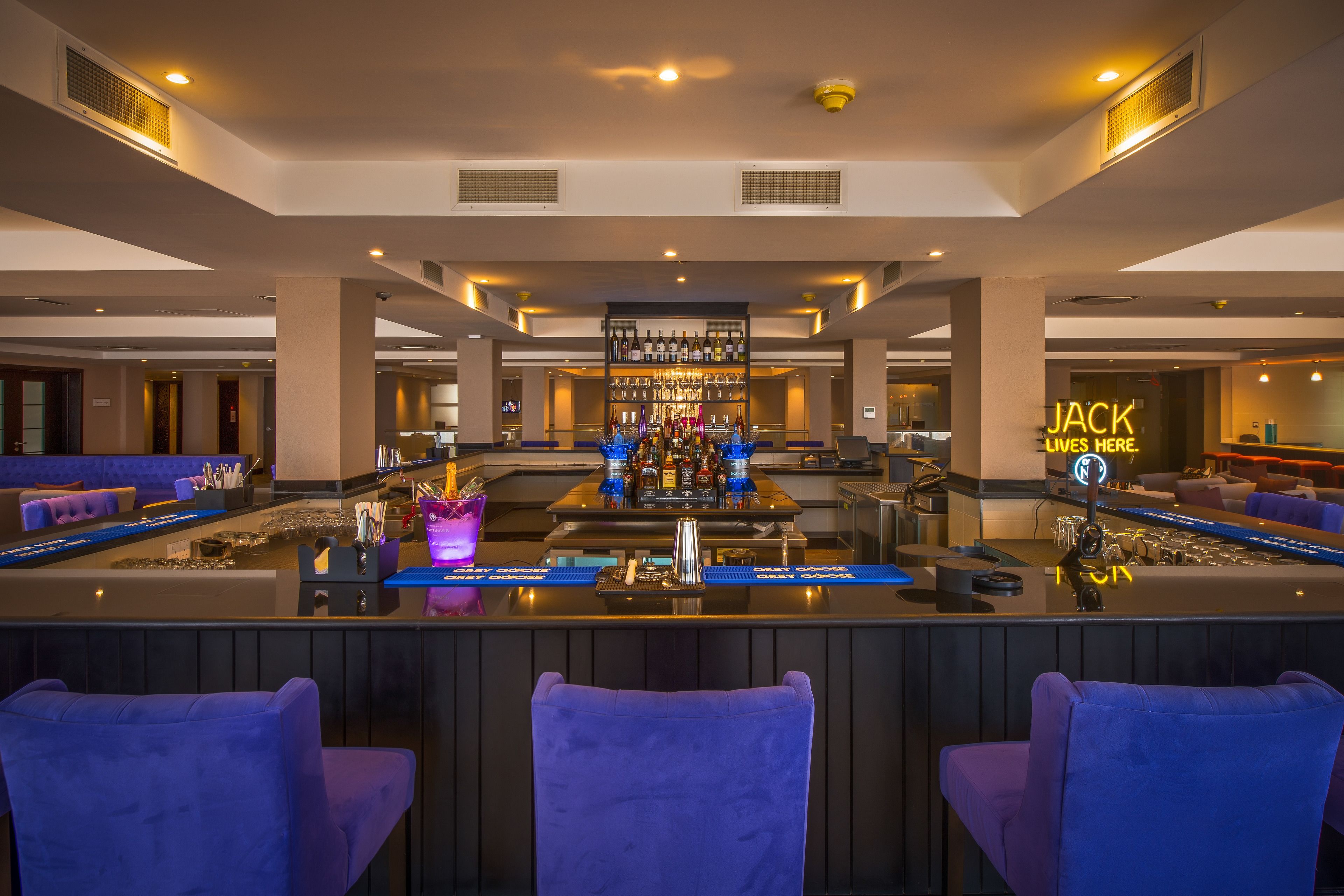 Un espace bar avec un comptoir, des tabourets de bar et un panneau lumineux au néon.