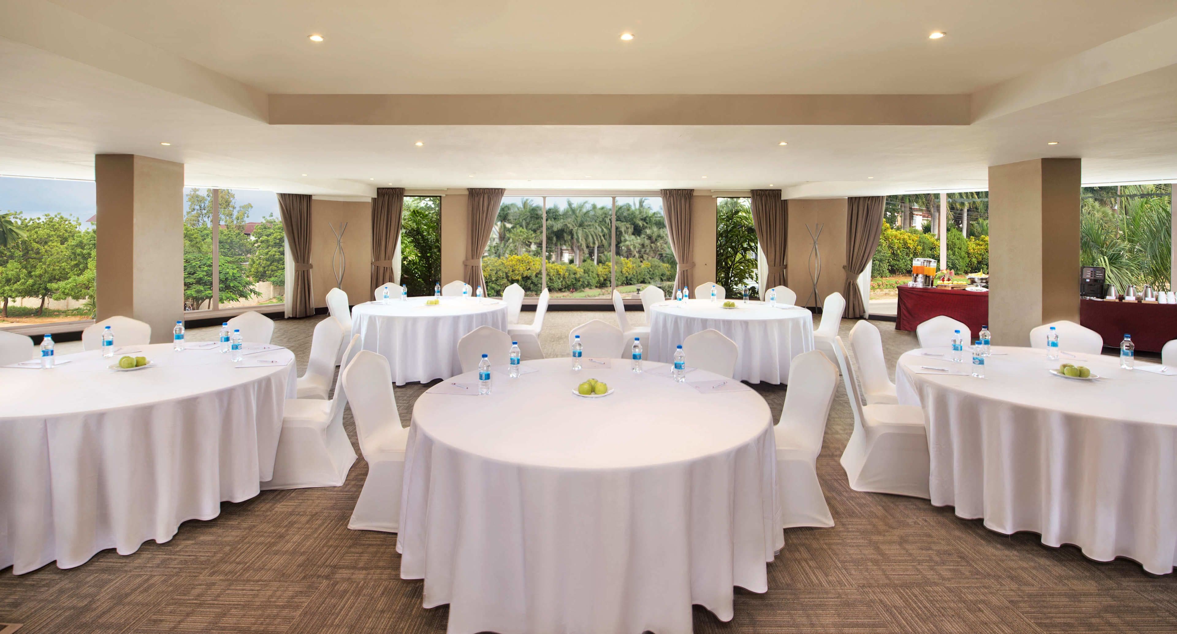 Un salón de conferencias con varias mesas redondas, sillas blancas y botellas de agua.
