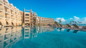 Un hotel con una piscina grande, tumbonas y un cielo azul despejado.