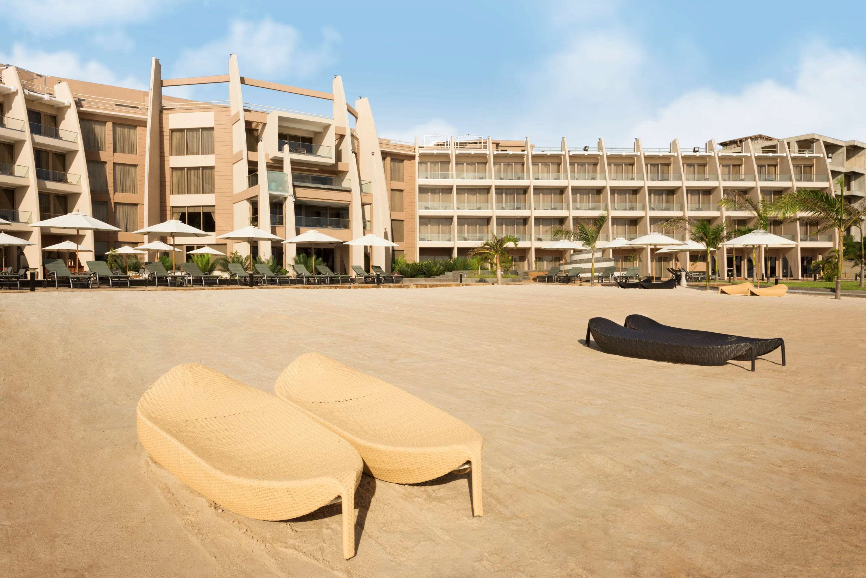Un hotel con varios pisos, zona de estar al aire libre con sombrillas y una playa de arena con sillones de descanso.