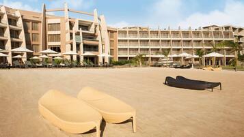 A hotel with multiple floors, outdoor seating with umbrellas, and a sandy beach area with lounge chairs.