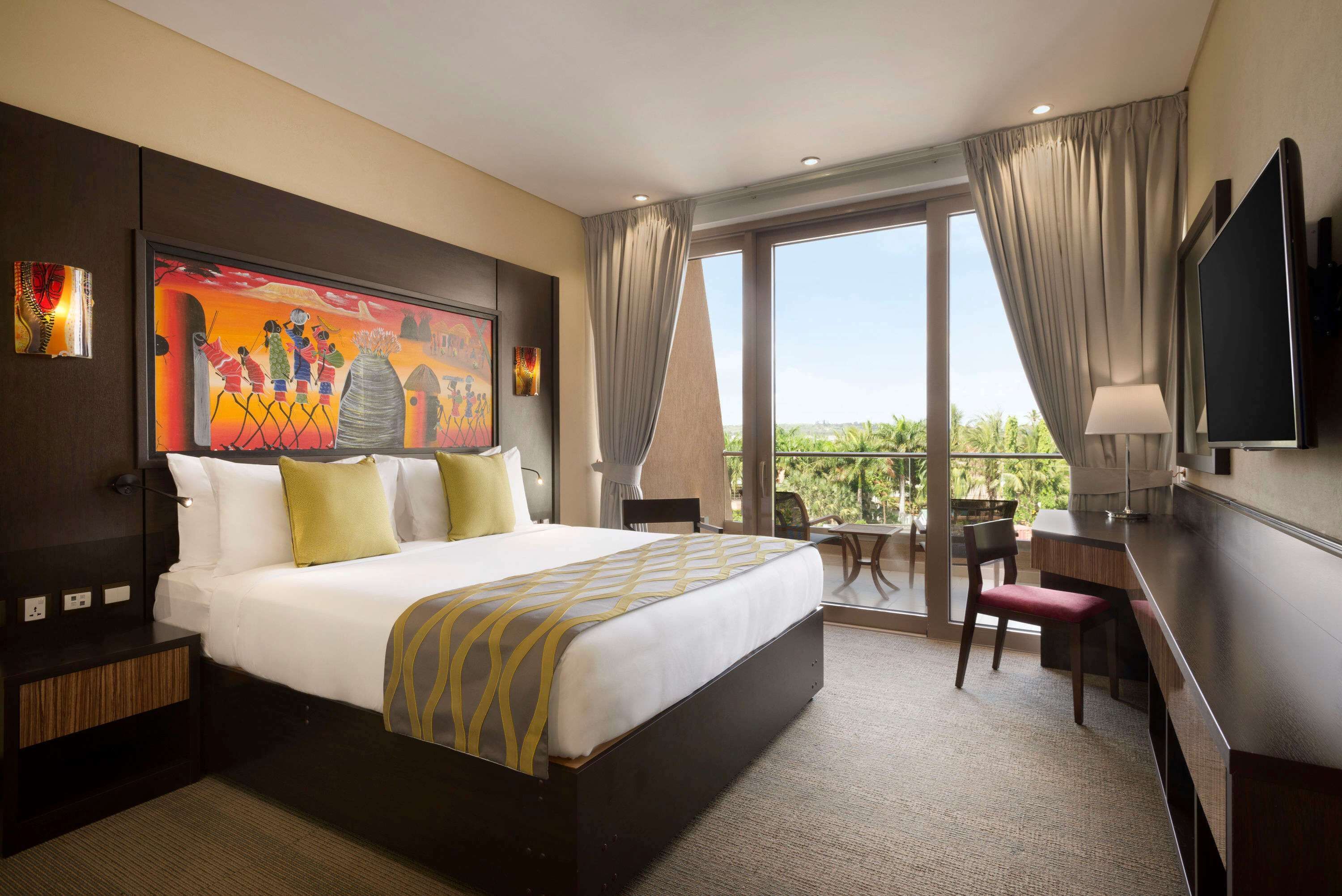 Une chambre d’hôtel avec un grand lit, un bureau, une chaise, une télévision et un balcon avec vue.