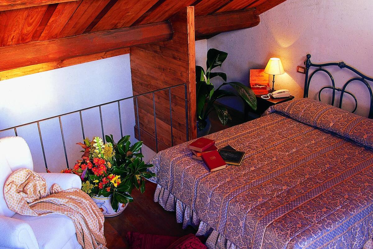 A bedroom with a bed, a chair, a nightstand, a lamp, and a potted plant.