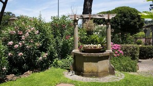 Ein Garten mit einer Steinfontäne, umgeben von üppiger Bepflanzung und blühenden Pflanzen.
