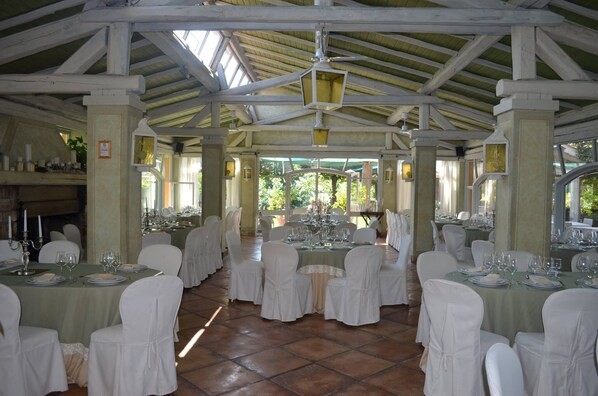 A covered dining area with tables set for a meal, white chairs, and a high ceiling with wooden beams. - La Locanda dei Ciocca (Grottaferrata)