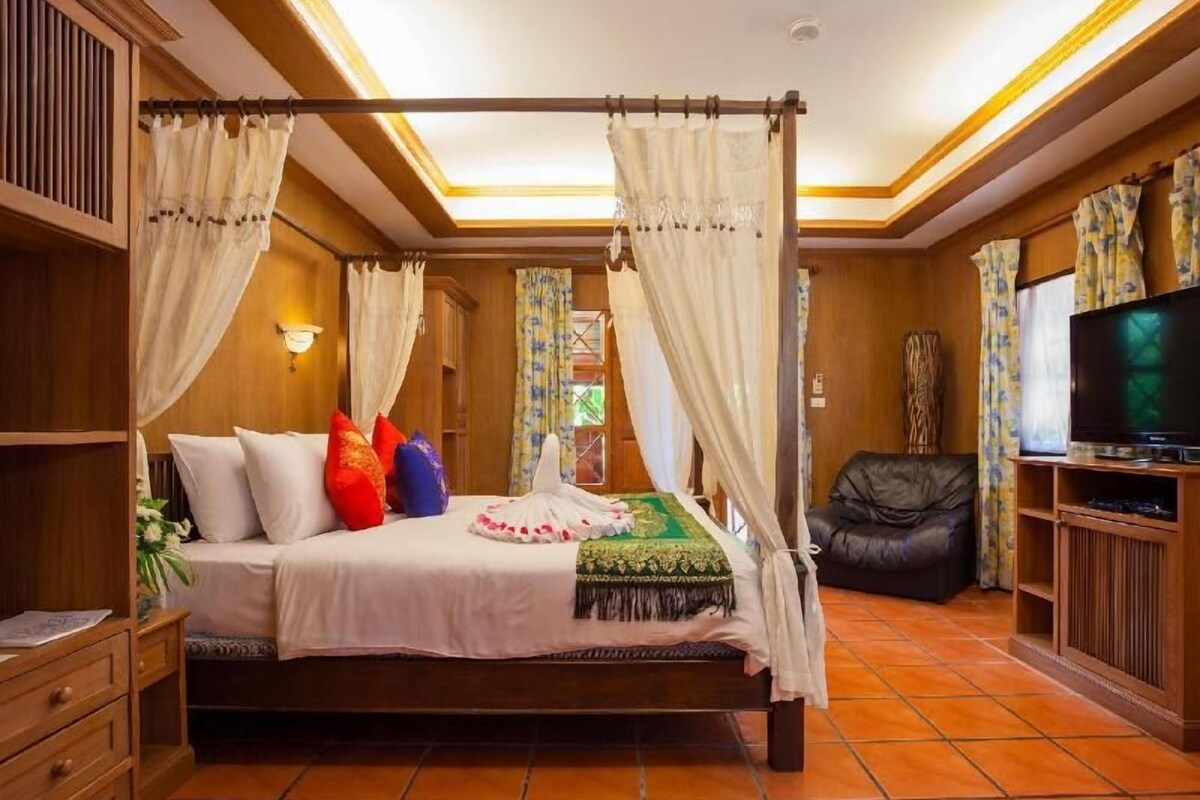 A four-poster bed with a canopy, a television, and a leather chair in a room with wooden walls and tiled flooring.