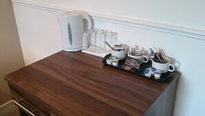 A small wooden desk with a white kettle, a tray with cups and a mug, and a coffee machine. - Livingston Lodge Hotel (Livingston)