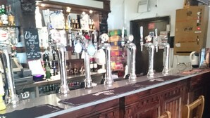 A bar with wooden stools and a bar counter with multiple taps. - Livingston Lodge Hotel (Livingston)