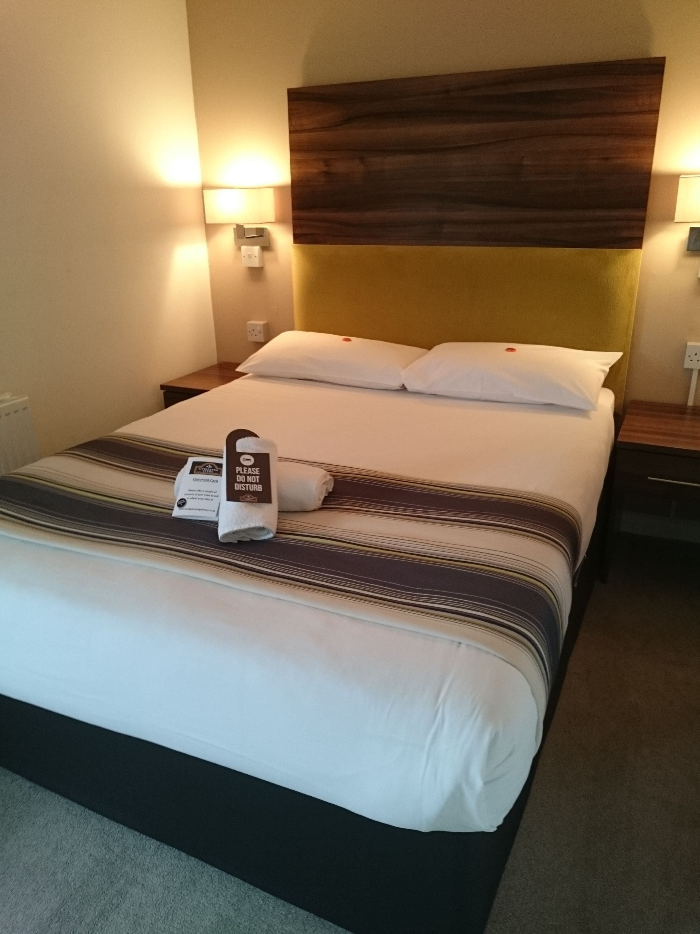 A neatly made bed with a comment card, two bedside tables, and wall-mounted lamps.