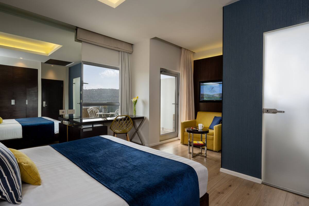 Habitación de hotel con cama, escritorio, silla, televisor y balcón con vistas.