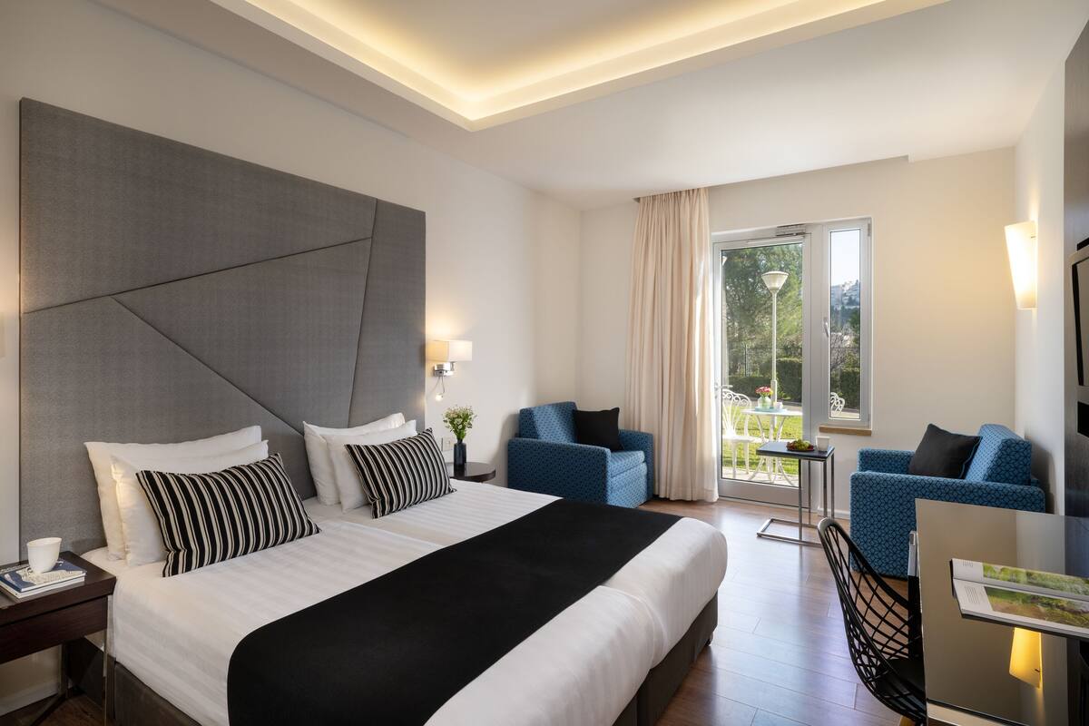 Habitación de hotel moderna con una cama grande, dos sillones, una mesita y un balcón con vistas.