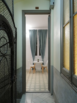 A hallway leading to a room with a small table and two chairs, a potted plant on the table, and a door with a number plate. - Casa Diagonal (Barcelona)